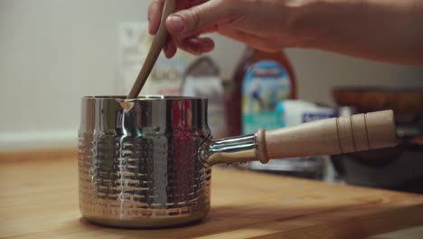 Woman-hand-stirring-water-in-a-metal-pan-on-top-of-cutting-board-with-a-wooden-spoon