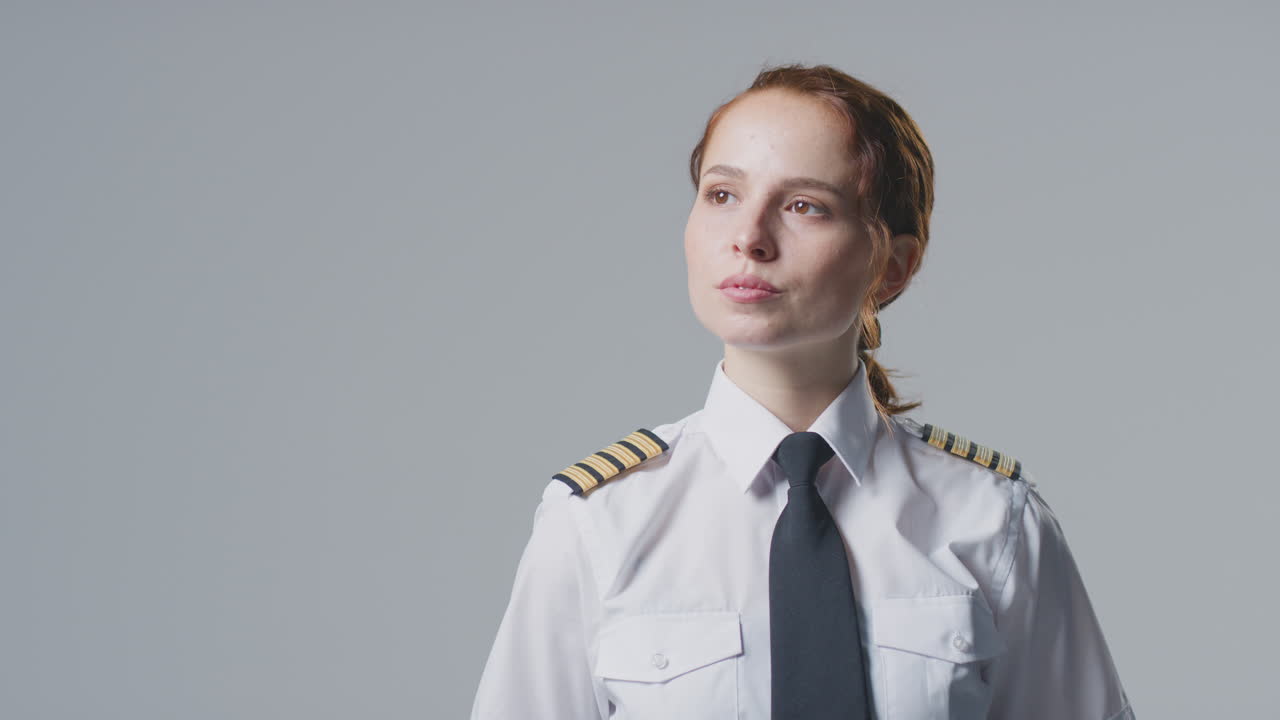 Studio Portrait Of Female Airline Pilot Or Ship Captain Looking Off Camera Against Plain Background