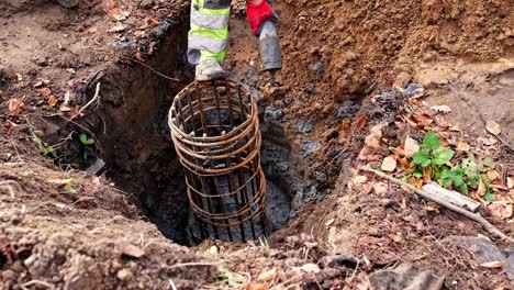 construction worker pouring liquid cement from pipeline filling up concrete foundation excavation with metal rods reinforcing cage