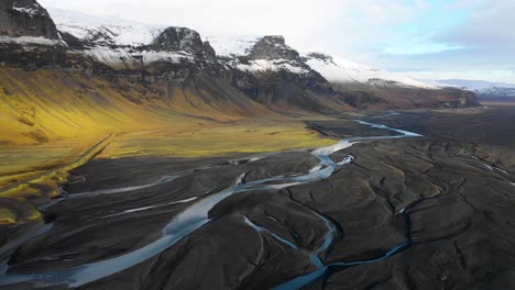 slow drone flight with autumn snowcapped mountains, icelandic braided river, black sand in southern iceland, vatnajokull area