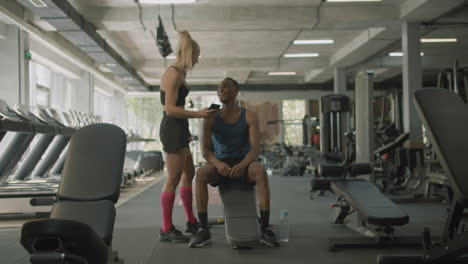 Caucasian-female-monitor-and-an-athletic-african-american-man-talking-in-the-gym.