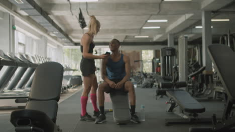 una mujer caucásica y un atlético afroamericano hablando en el gimnasio.