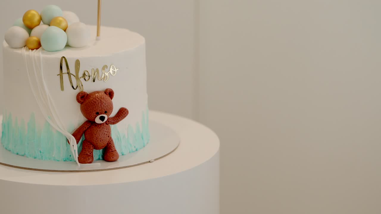 Custom baby cake with teddy bear and blue gold balloon decor featuring name Afonso in icing