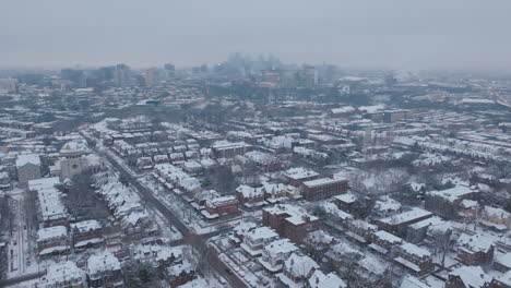 aerial drone footage of snow covered neighborhoods in west philadelphia with a foggy downtown skyline in the background.