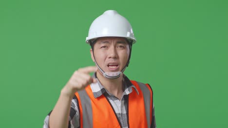 close up of angry asian male engineer with safety helmet shouting at someone while standing in the green screen background studio