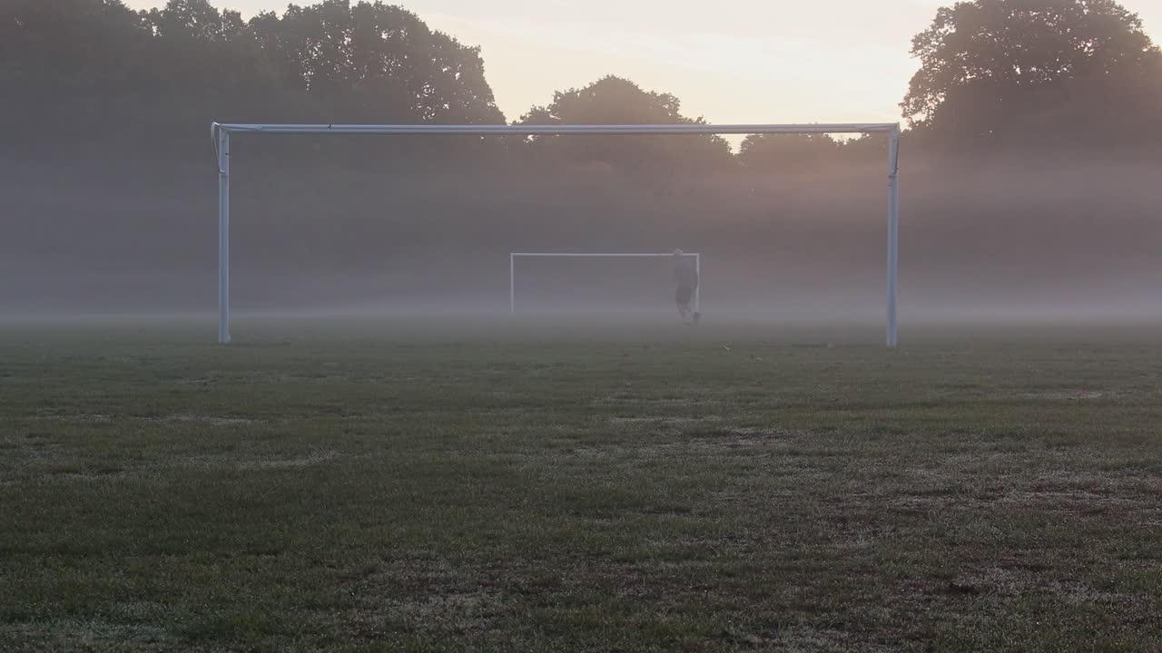 Man jogging past football goal posts in heavy fog, with his pet dog