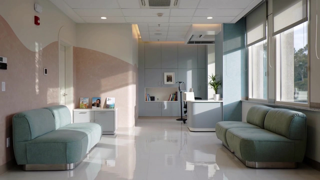 Klinikteki merkezi resepsiyon alanını gösteren hareketli kamera, resepsiyon masasını ve turkuaz kanepeleri ortaya çıkarıyor.