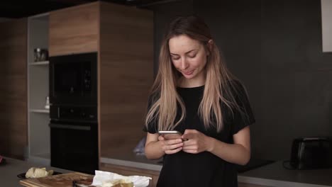 Shot-of-young-woman-using-her-mobile-phone-in-the-kitchen-at-home-in-the-morning