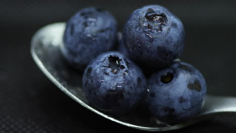 close up macro shot of blueberries laying on a teaspoon of splashed and spayed water on a dark background lying captured in slow motion