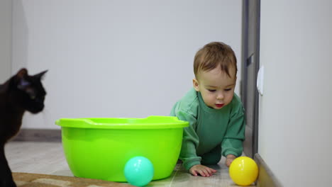 baby playing with balls in a green plastic bowl