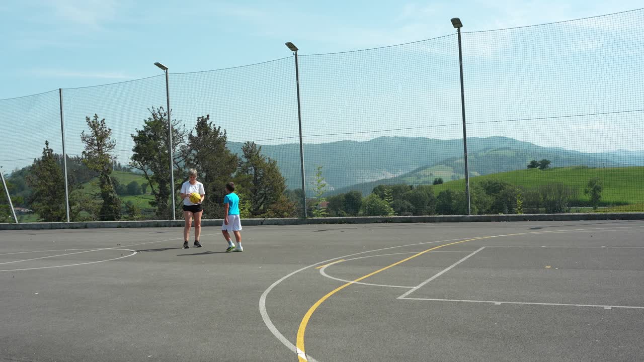 Dos chicos jugando al baloncesto en una cancha al aire libre con vistas a la montaña