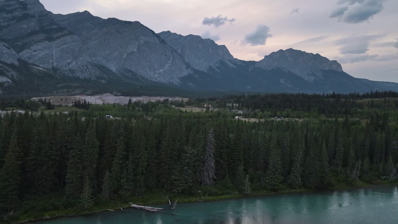 río kananaskis que fluye a través de un denso bosque exuberante debajo de las impresionantes montañas rocosas a la hora azul en alberta, canadá