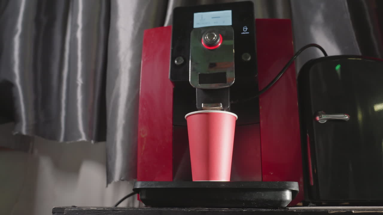 Coffee machine dispensing espresso into red paper cup, close-up view showing hand pressing button on machine. Modern espresso maker in action. Clean and focused scene of coffee preparation
