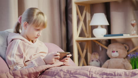 Ein-Kind-Spielt-Auf-Einem-Smartphone-In-Seinem-Schlafzimmer-Liegt-Im-Bett