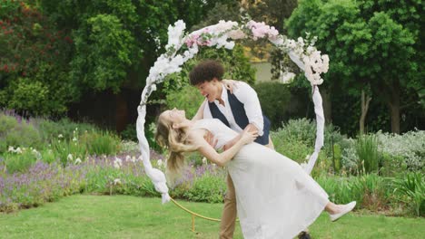 happy diverse couple dancing in garden on sunny day at wedding