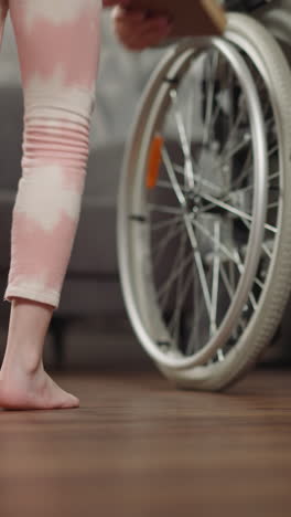 una hija cariñosa ayuda a su madre con discapacidad a recoger un libro tendido en el suelo. una niña en edad preescolar cuida a su mamá en silla de ruedas después de una cirugía de primer plano