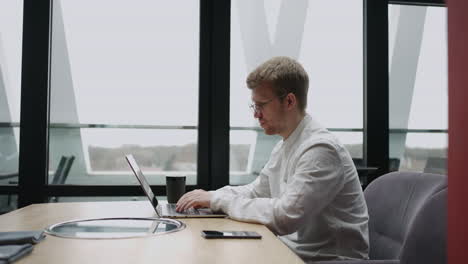 un hombre adulto está trabajando solo en una oficina moderna usando una computadora portátil con conexión inalámbrica a internet para buscar información