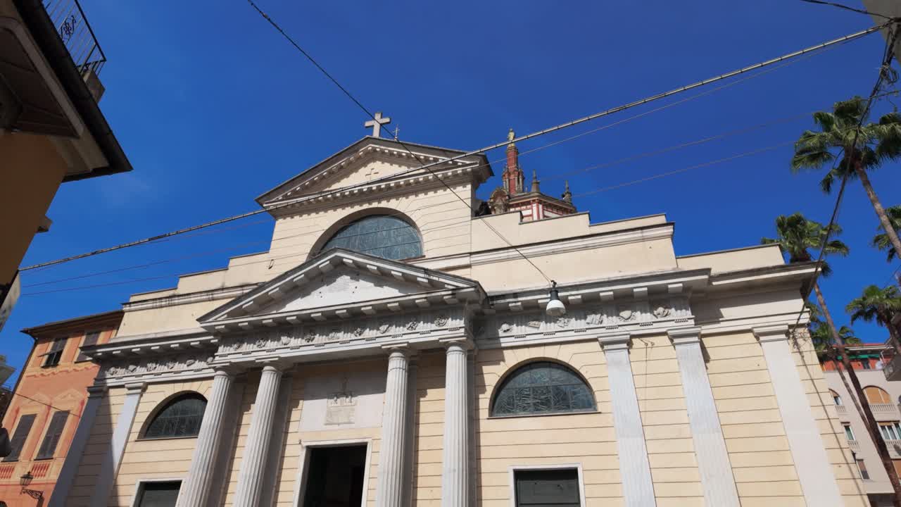 Splendide riprese grandangolari della Basilica dei Santi Gervasio e Protasio a Rapallo, Italia, sotto un cielo azzurro brillante. Classica facciata neoclassica, colonne imponenti e composizione con luce diurna calda.