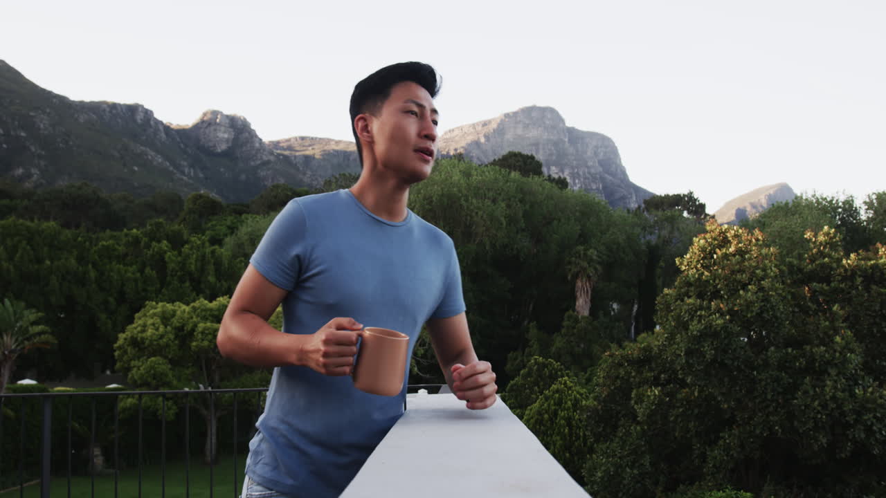 Asian man enjoying morning coffee on balcony with scenic mountain view, copy space