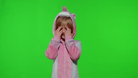 little blonde child in unicorn costume crying, wiping tears with her hands on chroma key background