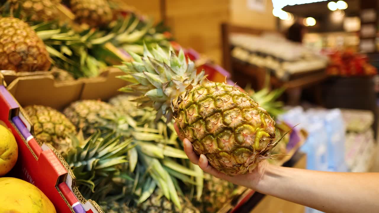 A person examines pineapples in a well-lit supermarket, focusing on freshness and quality in Gold Coast, Australia