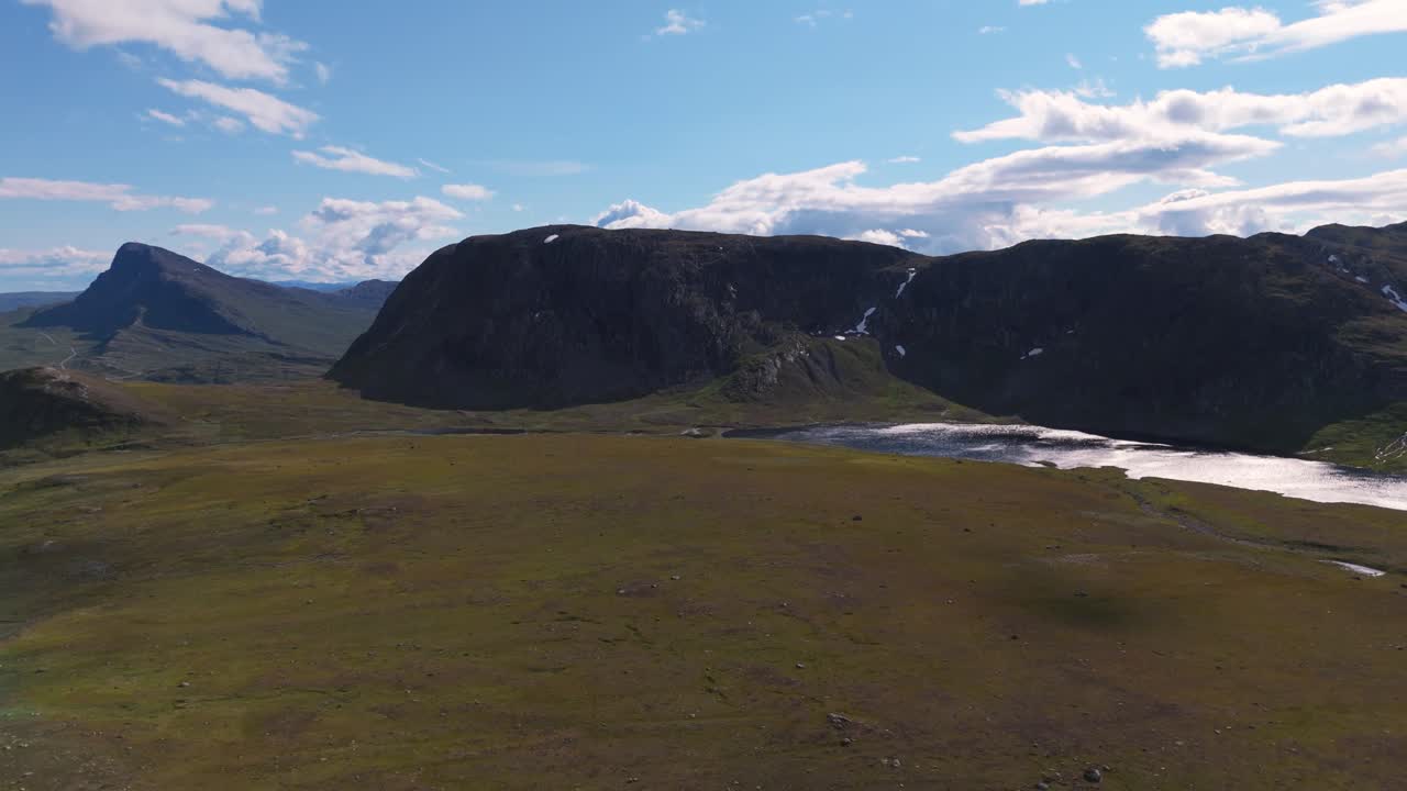 Ilmakuva vuoristojärvestä, joka heijastaa sinistä taivasta aurinkoisena päivänä muutamien pilvien kera.