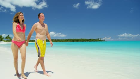 young caucasian couple walking on white sand beach