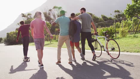 happy diverse male friends walking with bicycle and talking on sunny day