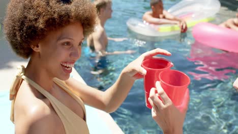 un grupo feliz y diverso de amigos con inflables y bebiendo bebidas en una fiesta en la piscina en verano.