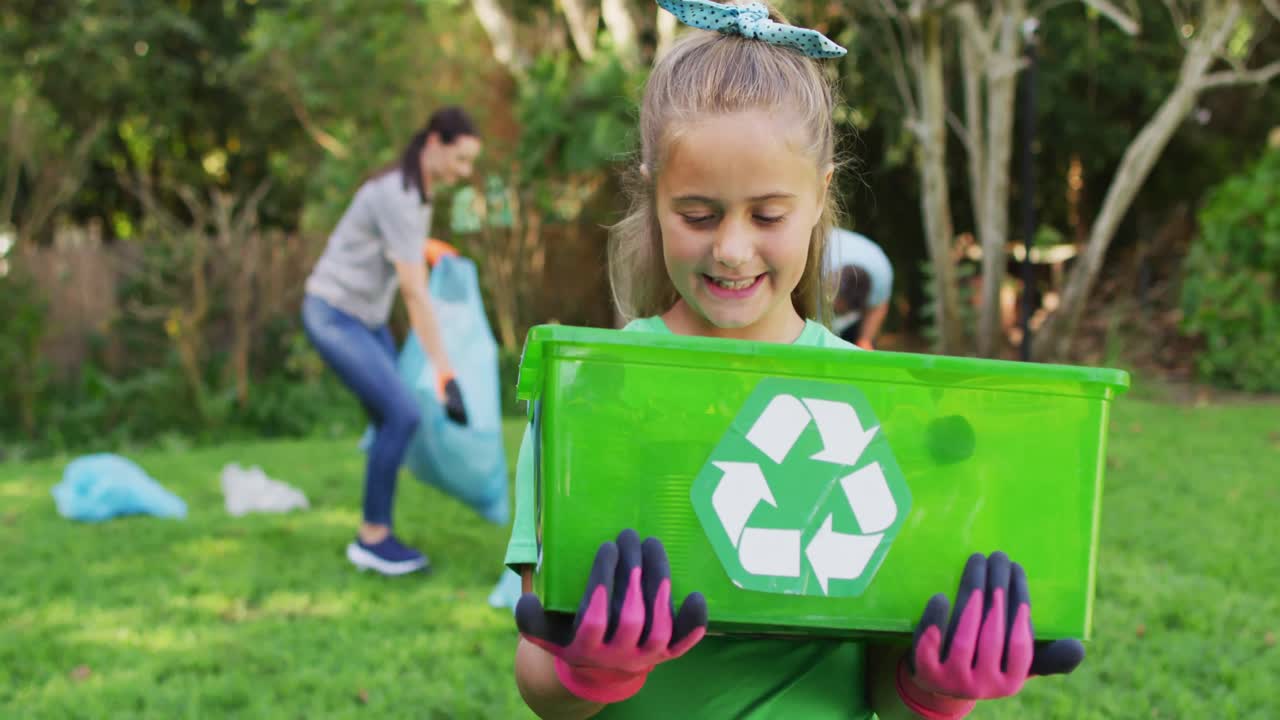 hija caucásica sonriente al aire libre sosteniendo una caja de reciclaje, recolectando residuos plásticos con los padres