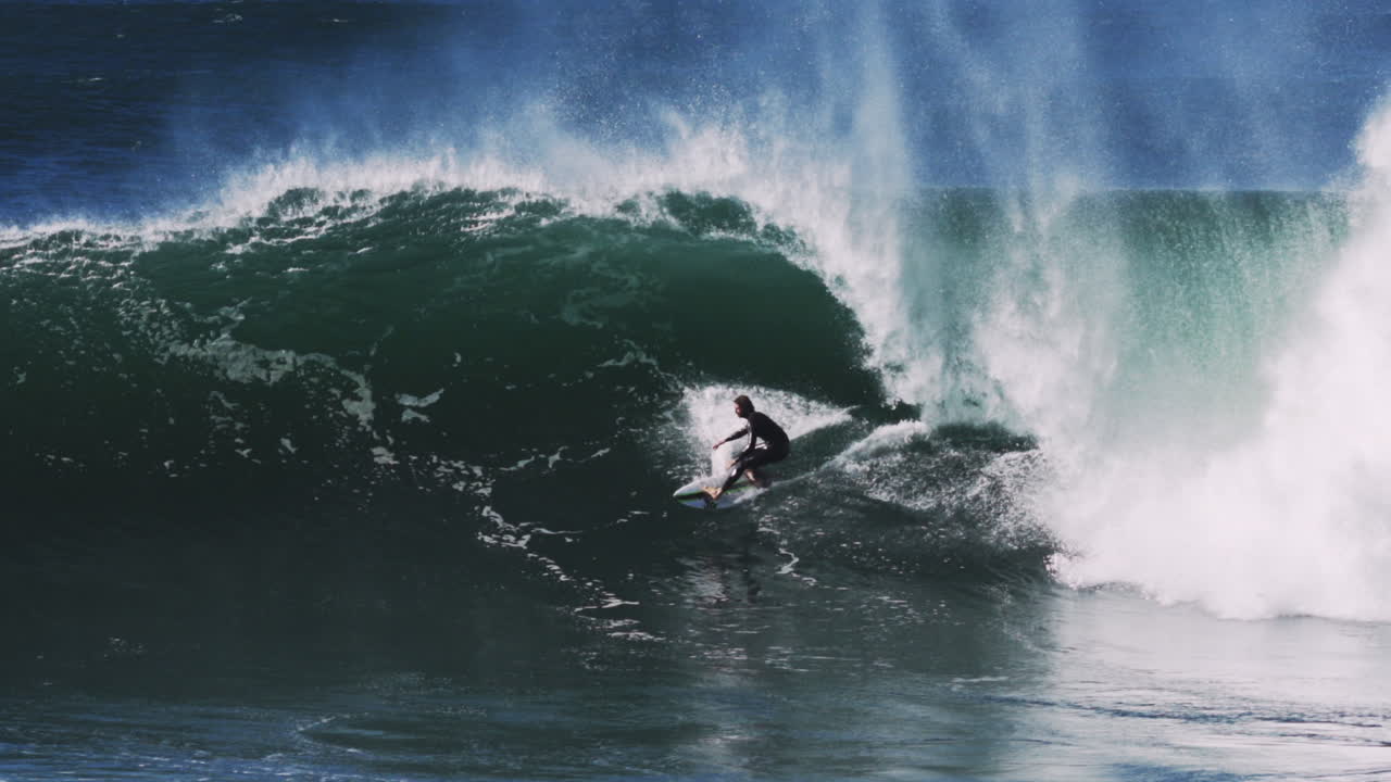 Tubo dell'onda che si arrotola rifrange la luce attraverso il labbro traslucido mentre il surfista taglia la conca.