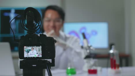 asian scientist researching in the laboratory with a microscope and speaking to the camera