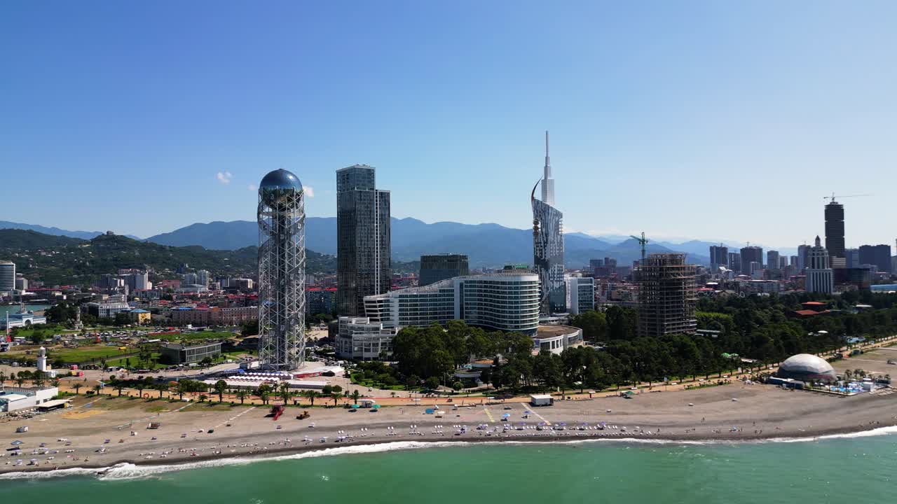 Aerial Drone Footage Captures Batumi, Georgia On A Sunny Summer Day. The Vibrant Beach Scene Showcases People Sunbathing, Modern Buildings, And The Green Hues Of The Black Sea.