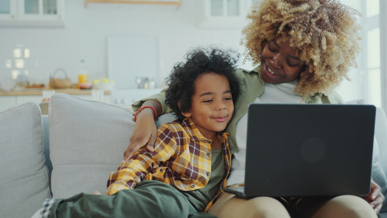 Happy Mother and Little Son Watching Cartoon on Laptop on Couch at Home