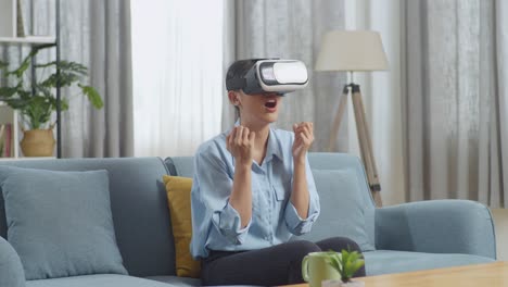 mujer asiática usando gafas de realidad virtual mientras está sentada en el sofá en la sala de estar