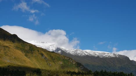 panorama shot of snowy mountains during sunny day with blue sky and rural landscape during hiking at rob roy glacier track in new zealand