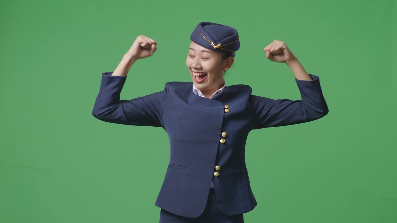 아시아 여성 승무원이 녹색 스크린 배경 스튜디오에 서서 미소 짓고 팔꿈치를 구부리고 있습니다.