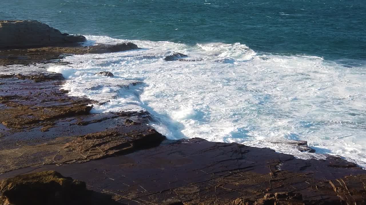 Ocean waves are crashing onto rocky shore while camera pans from right to left in ultra slow motion.