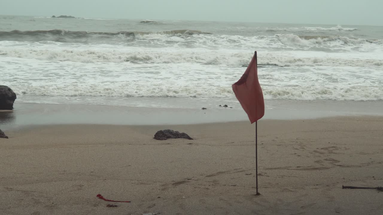 해변과 인명구조원은 파도가 배경에 부딪히는 모래에 붉은 깃발을 꽂았다고 경고합니다.