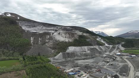 rising aerial view of limestone and quarry mining site for between molde and kristiansund in norway - aerial showing heavy machinery and equipment at job site and damaged mountain in background