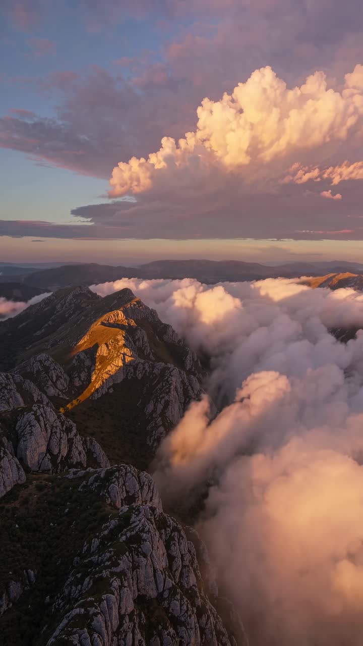 Aerial video shot at dawn captures rugged mountain peaks shrouded in mist, with a dramatic sky