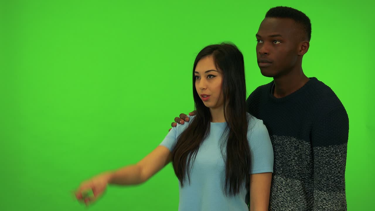 A young Asian woman and a young black man point at and talk about their surroundings - green screen studio