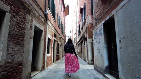 following a woman tourist walking through narrow alleys in venice, italy