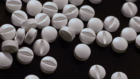 bunch of white pills scattered on a black surface, united states opioid crisis