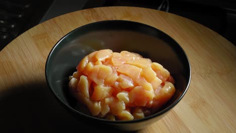 putting chopped and uncooked skinless chicken breast meat into bowl