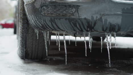 close-up da luz de nevoeiro do carro envolto em gelo com icebergs pendurados, exibindo efeitos de inverno severos nos exteriores do veículo e um carro vermelho desfocado no fundo