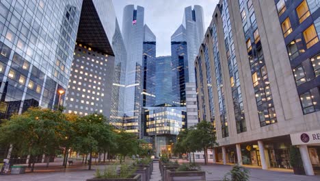 Vista-Timelapse-De-Un-Paisaje-Urbano-Moderno-Con-Edificios-Futuristas-De-Vidrio-Y-Acero,-Un-Parque-En-Primer-Plano-Y-El-Edificio-Renacentista