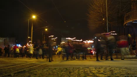 Timelapse-of-people-going-in-a-torchlight-procession-over-the-Liepaja-tram-bridge-on-Lacplesa-day-,-city-landscape,-traffic-light-streaks,-wide-shot