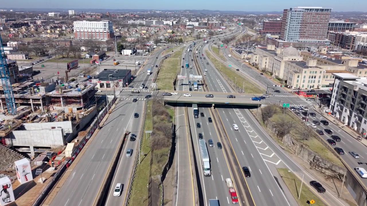 Pemandangan drone siang hari yang terbang maju di atas Interstate 40 di The Gulch, Nashville, Tennessee, mengungkapkan jalan raya multi-jalur yang sibuk, konstruksi di dekatnya, dan cakrawala kota