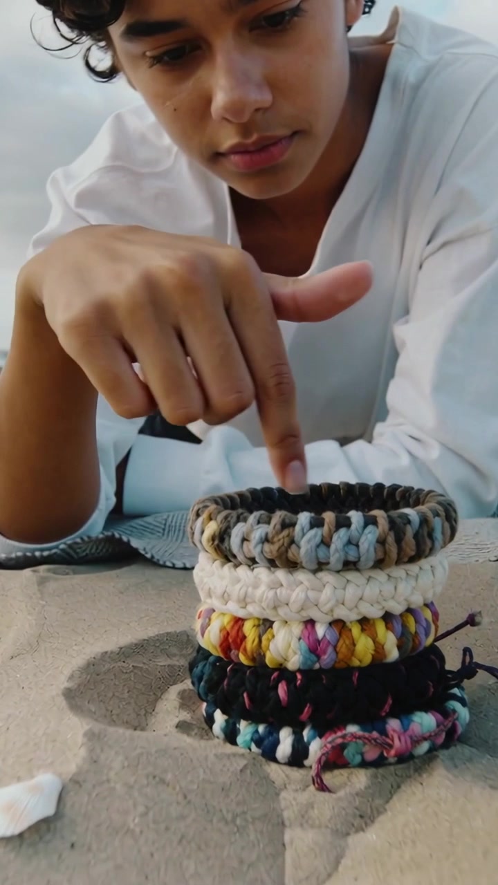 Vertical video: Seeing stacked bracelets, teen in white top leaning on sand, studying, tapping ring